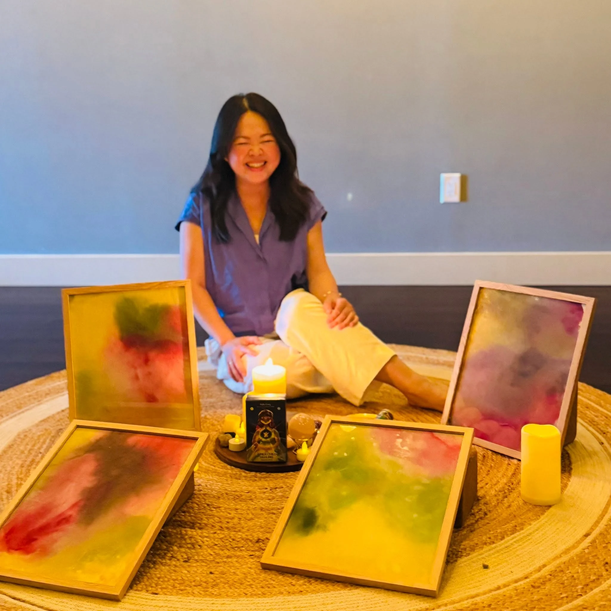 Kylie sitting with colorful original intuitive paintings during an Auric and Soul Colors creative session